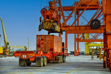 Port logistics and container terminal operations. Industrial gantry crane loading a shipping container onto a heavy-duty semi-truck trailer at a busy maritime terminal, global trade and transportation © Kosal