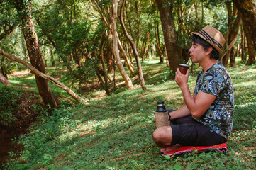 hombre con sombrero marrón bebiendo un delicioso mate en medio de la naturaleza con muchos árboles y plantas © Daniel