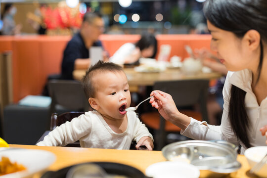 Mother feeding baby at restaurant table indoors