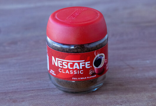 Kishoreganj, Bangladesh - 05 February, 2026 - A jar of Nescafe Classic instant coffee with a red lid on a wooden surface. A product shot showing bold flavor granules for morning caffeine energy