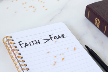 Faith over fear, handwritten text in notebook with mustard seeds and holy bible book. Christian biblical concept. Close-up.