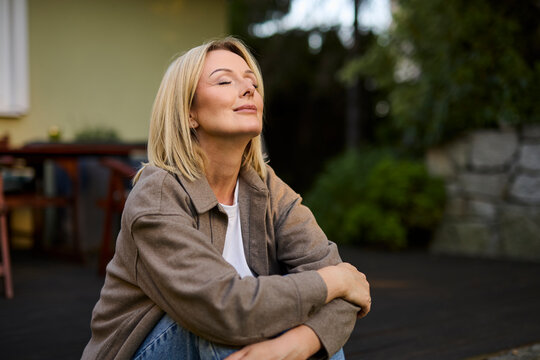 Relaxed woman sitting in back patio breathing peacefully outdoors
