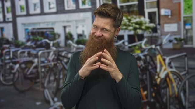 Smiling bearded man steepling fingers by a row of rental bicycles parked on a busy street under natural daylight; mischief.
