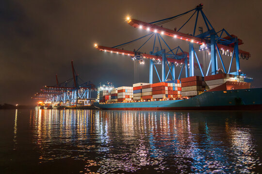 Container terminal at night in Hamburg harbor with cargo ship and cranes