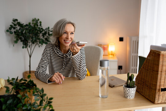 Smiling woman using mobile phone for voice message at home office