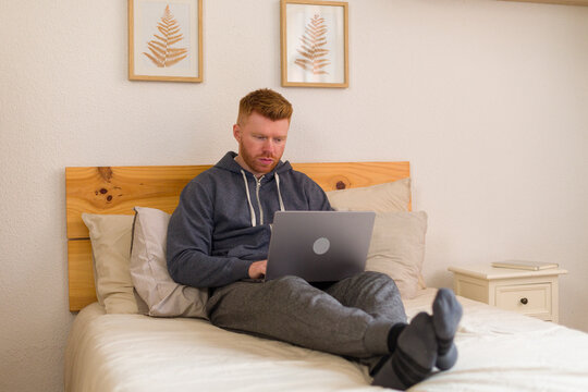 Man working remotely on laptop in bed in a comfortable bedroom