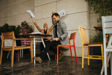 Fototapeta premium Two business partners cheer at a cafe table, papers flying as they celebrate a successful discussion.