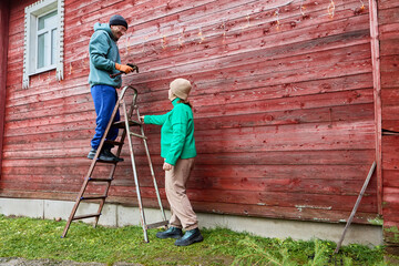 Getting ready for Christmas married couple adorns wooden house with festive decor.