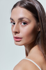 Graceful young woman gazes confidently with radiant beauty against a minimalist backdrop