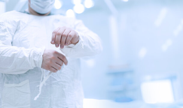 Person fastening surgical gown sleeves in operating room