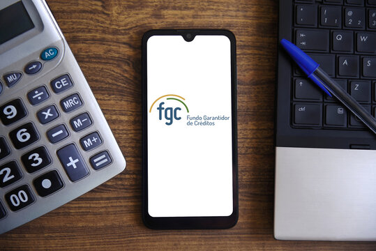 Logo of the FGC (Credit Guarantee Fund), on a smartphone screen with a laptop and calculator. A private association, part of the National Financial System (SFN), that works to increase trust. 