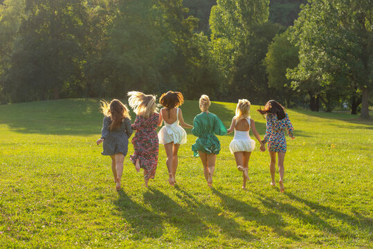 Group of women running barefoot through grass in park on a sunny day of summer