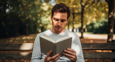 Fototapeta premium Young man with freckles reading book outdoors on wooden bench in autumn park calm sunlight peaceful atmosphere natural lifestyle concept
