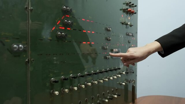 A person's hand is reaching out to a green panel with many buttons and switches