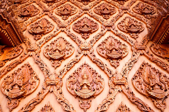 Intricate traditional wood carving of Deva clasping hands figure and Kanok patterns on teak wooden wall of Thai temple, showcasing exquisite Asian craftsmanship and cultural heritage