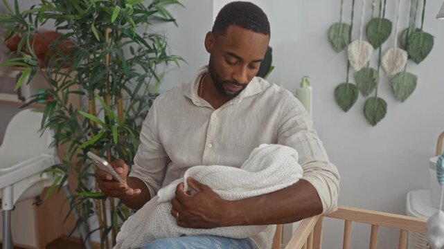 Man holds swaddled baby in crib inside building while checking phone with gentle hands; tenderness fatherhood bonding.