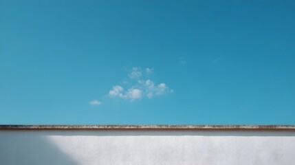 A minimalist composition featuring a textured white wall with a concrete border against a vibrant clear blue sky with a single small cloud