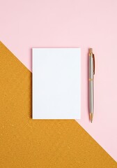 Blank notepad and silver pen resting on a dual toned pink and gold background
