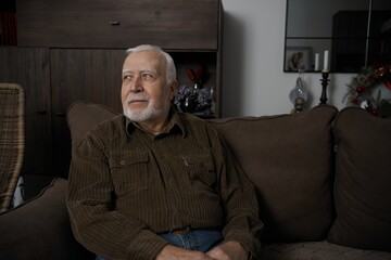 Fototapeta premium Senior man sitting on a couch looking thoughtfully in a cozy living room during the day