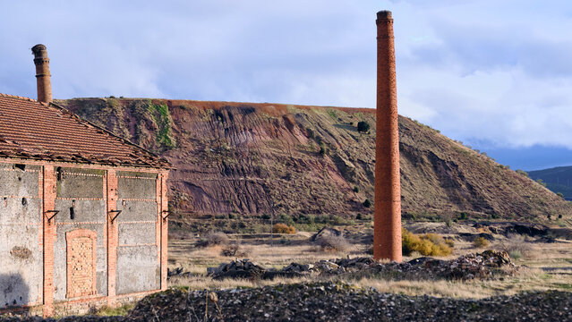 View of the stark contrast between the aged brick structures and the towering red earth, a landscape scarred yet strangely beautiful, Puertollano, Castile-La Mancha, Spain.
