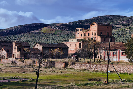 View of the old coal loading facility standing silently against the mountainous backdrop, brick buildings fading into the landscape, Puertollano, Spain.