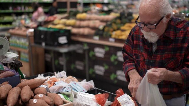 Elderly man selects fresh produce and places it in a bag while shopping in a grocery store in the afternoon.