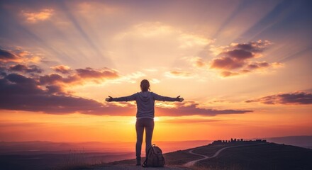 Fototapeta premium A woman standing on a mountain top with her arms outstretched, enjoying the sunset.