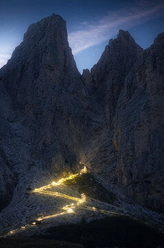 View of a winding path of lights climbs a steep, rugged mountain under a twilight sky, illuminating the dark stone and guiding adventurers, Trentino-South Tyrol, Italy.