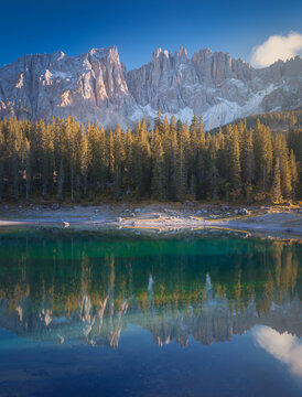 View of the serene Lago di Carezza mirroring the rugged Dolomites and lush forest under a clear blue sky, creating a tranquil landscape, Trentino-South Tyrol, Italy.