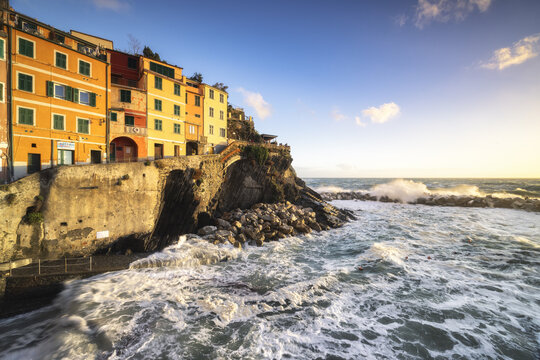 View of colorful buildings clinging to the rugged coastline as waves crash against the rocky shore, creating a mesmerizing scene, Riomaggiore, Liguria, Italy.