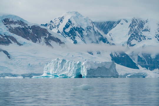 View of an iceberg floats serenely in the frigid water, set against a backdrop of towering snow-capped mountains, Portal Point, Graham Land, Antarctica.