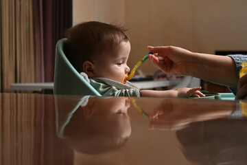 young child in a chair eating with a spoon against the light
