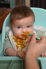 young child in a chair eating clumsily with a spoon
