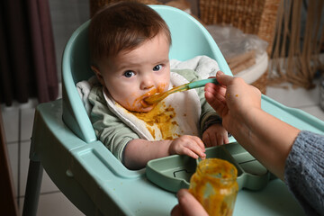 young child in a chair eating clumsily with a spoon
