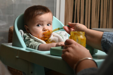 young child in a chair eating clumsily with a spoon