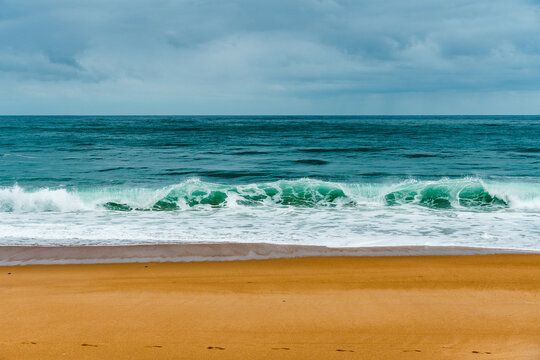Waves crashing on the sandy beach in Labenne, Landes, France, on a cloudy day.