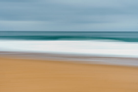 Long exposure shot of waves crashing on the sandy beach in Labenne, Landes, France, on a cloudy day.