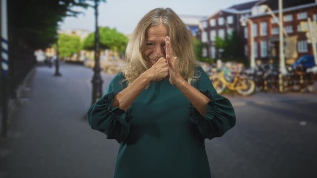 Senior woman presses palms together and performs varied hand gestures on a city street with bicycles and buildings in view; expressive thoughtful.