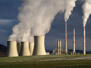Coal-fired power plant with cooling towers and chimneys emitting thick steam and smoke against dark storm sky
