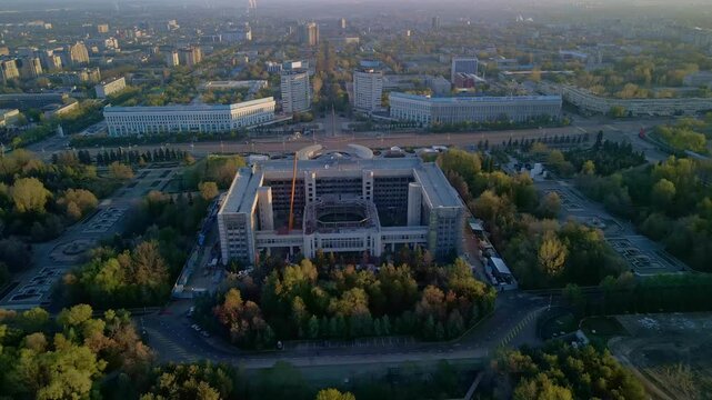 Cinematic aerial drone flight over Almaty city skyline. Panoramic view of modern skyscrapers and historical buildings with snow-capped Tian Shan mountains in Kazakhstan.