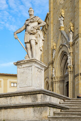 Fototapeta premium Arezzo, Italy. Marble statue of Guido Tarlati on a stone pedestal in front of the Cathedral of Saints Peter and Donatus in Arezzo, Tuscany, with Gothic ornate portal and statues in background.