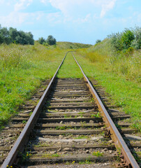 Old abandoned railway tracks disappearing into the distance among green fields