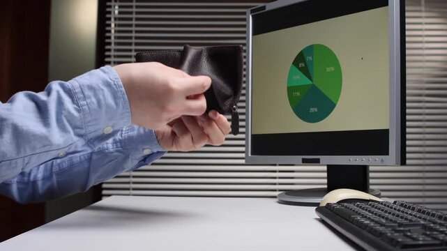 Person's hands opening an empty wallet at a desk, indicating financial struggles and budget limitations, with a computer screen displaying an expense pie chart in the background