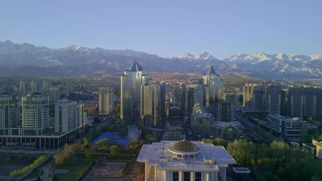 Aerial sunrise view of Almaty city skyline, Kazakhstan. Urban architecture with modern buildings and morning mist under a soft dawn sky. 4K drone footage.