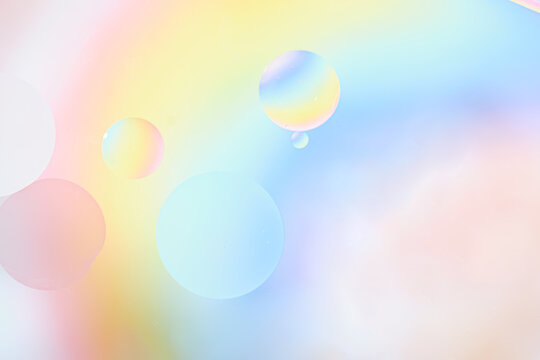 Horizontal macro shot of glossy translucent bubbles in iridescent pastel rainbow hues pink, blue, yellow, green floating over soft gradient background