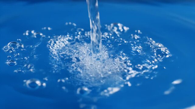 Water Ripples and Bubbles in Blue - A stream of clear water pours into a pool of bright blue liquid, creating a flurry of ripples and bubbles on the surface.