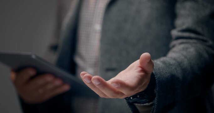 Unrecognizable businessman holding a digital tablet while offering an open hand gesture, representing online consulting, customer support, and digital services. Copy space and shallow depth of field.