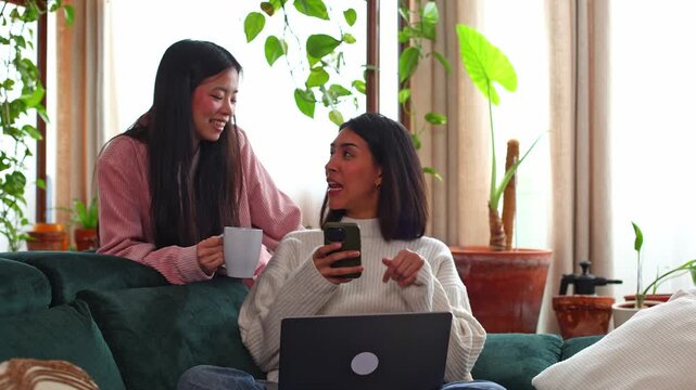Two female friends laughing and talking on the couch