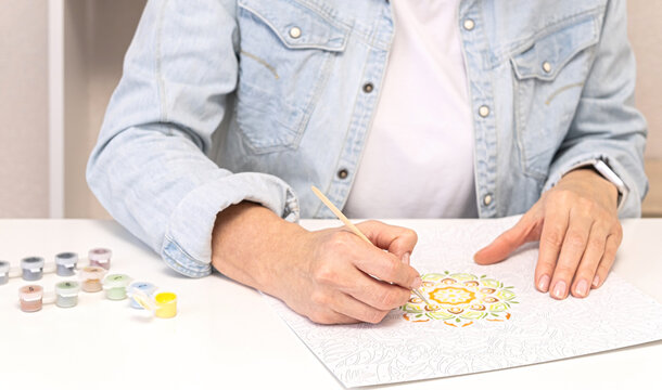 Woman practices mindful adult coloring with brush and acrylic paints