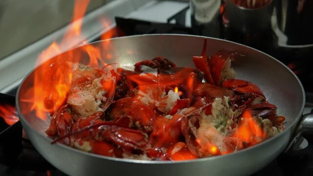 A high flame rises above the pan, searing the lobster shells. A professional chef flamb&eacute;s a lobster in a pan.